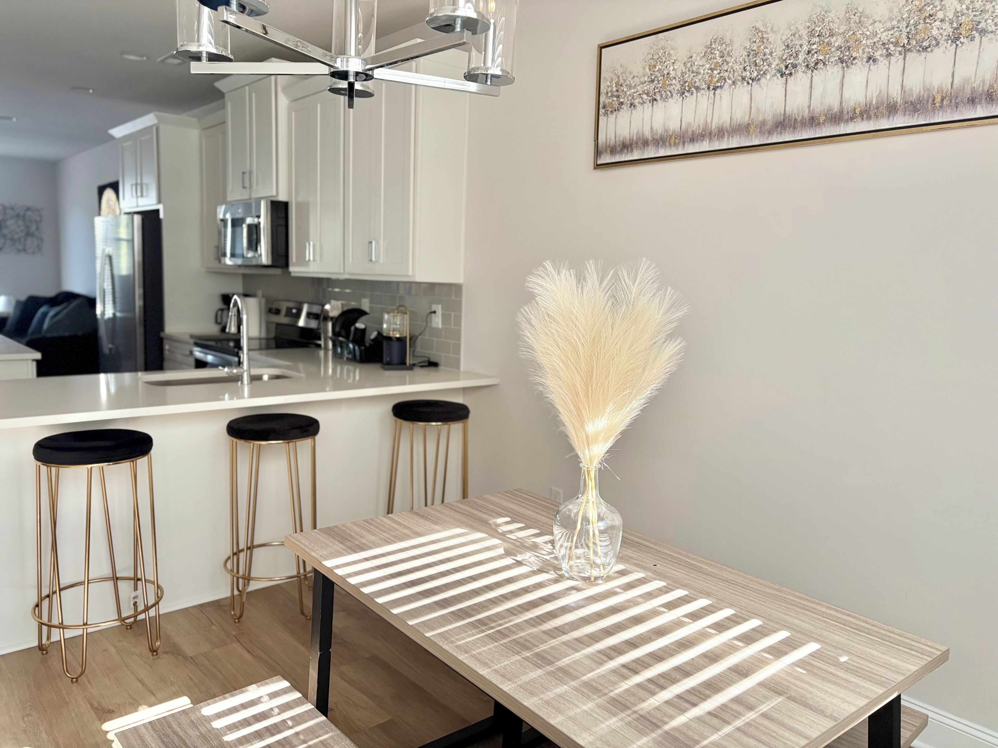 A modern kitchen with white cabinets, a stainless steel refrigerator, and a dining area with a wooden table and bar stools.