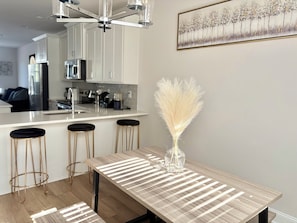 A modern kitchen with white cabinets, a stainless steel refrigerator, and a dining area with a wooden table and bar stools. - 3-bedroom Townhome in Serene Uptown Charlotte (Charlotte)