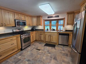 Eine Küche mit Holzausstattung, einem Edelstahl-Kühlschrank, einer Mikrowelle, einem Backofen und einem Geschirrspüler.