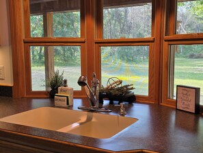 A kitchen with a sink, wooden window frames, and a view of a yard. - Club 39 Lodge Private 5 Acres + Hot Tub (Luther)