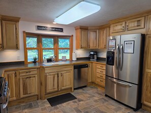 Cocina con armarios de madera, refrigerador de acero inoxidable, cafetera y ventana con vista a follaje.