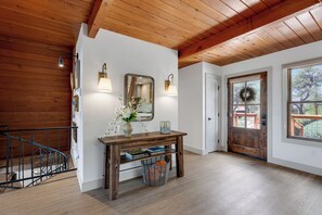 A wooden staircase, a wooden console table with a mirror, wall sconces, a door with a wreath, and a large window. - River Frontage•Pet Friendly•Renovated Luxury (Howard)