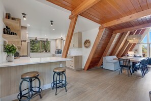 A modern kitchen with a central island, bar stools, and a dining area with a high ceiling and exposed beams. - River Frontage•Pet Friendly•Renovated Luxury (Howard)