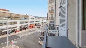 Ein Balkon mit Blick auf eine Straße mit Geschäften, einem klaren Himmel und einem Gebäude mit einem Balkon.