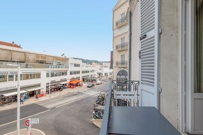 Ein Balkon mit Blick auf eine Straße mit Geschäften, einem klaren Himmel und einem Gebäude mit einem Balkon.