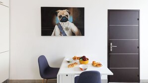 Ein Zimmer mit einem weißen Tisch, zwei blauen Stühlen, einer dunklen Tür und einem gerahmten Bild von einem Hund an der Wand.