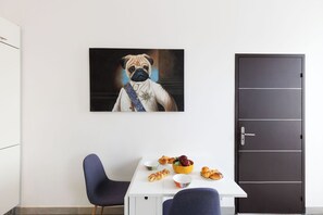Ein Zimmer mit einem weißen Tisch, zwei blauen Stühlen, einer dunklen Tür und einem gerahmten Bild von einem Hund an der Wand.