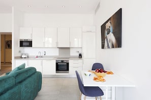 A modern kitchen with white cabinets, a dining table with chairs, and a painting on the wall. - Upstays Spacious 77m² T3 Apartment with Terrace (Cannes)