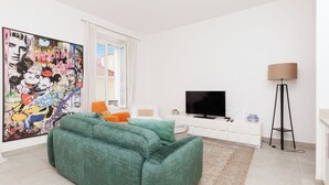 Ein modernes Wohnzimmer mit einem grünen Sofa, einem Flachbildfernseher, einer Stehlampe und einem großen abstrakten Gemälde an der Wand.