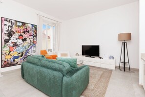 Ein modernes Wohnzimmer mit einem grünen Sofa, einem Flachbildfernseher, einer Stehlampe und einem großen abstrakten Gemälde an der Wand.