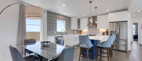A modern kitchen with a central island, stainless steel appliances, and a dining area with a glass table and chairs.