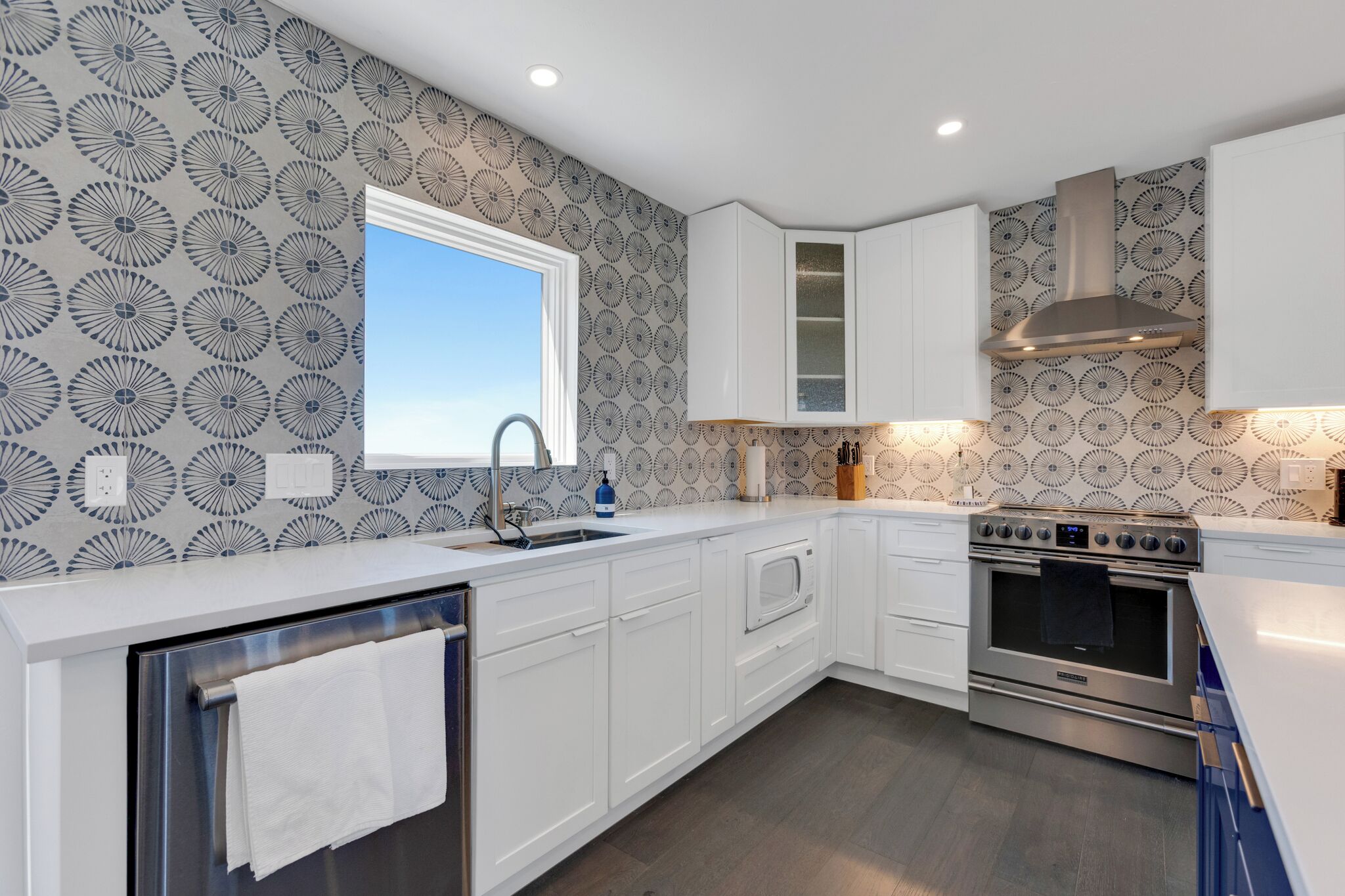A modern kitchen with white cabinetry, a stainless steel range hood, and a window providing natural light.