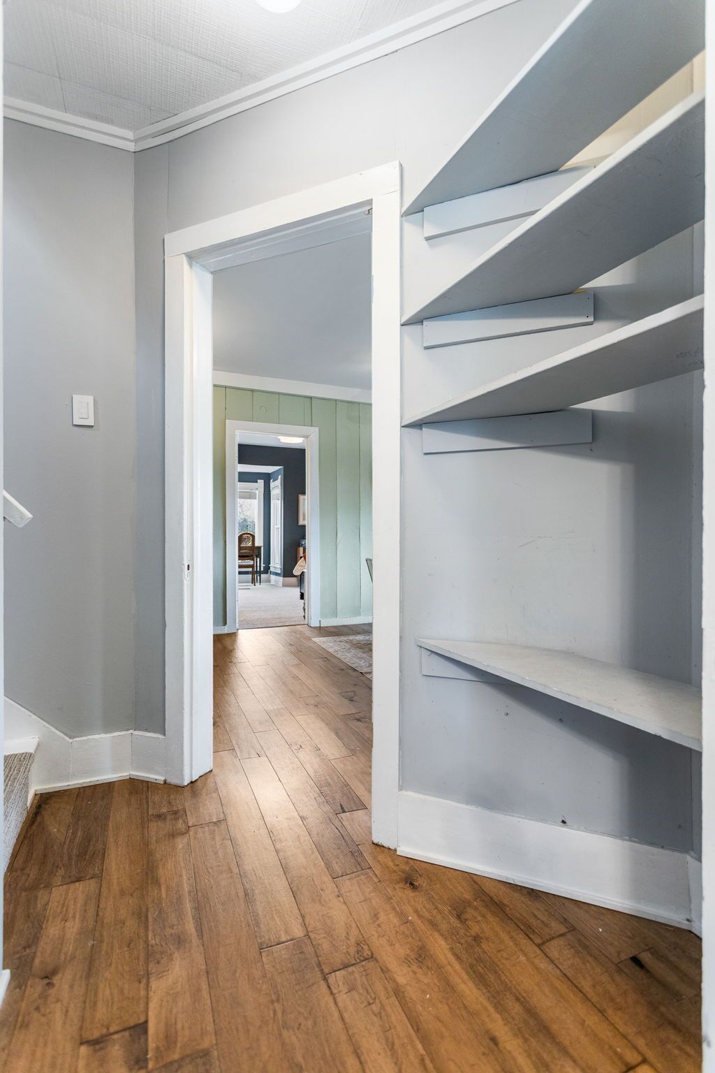 Un pasillo con piso de madera, una puerta blanca y una escalera con barandillas blancas.