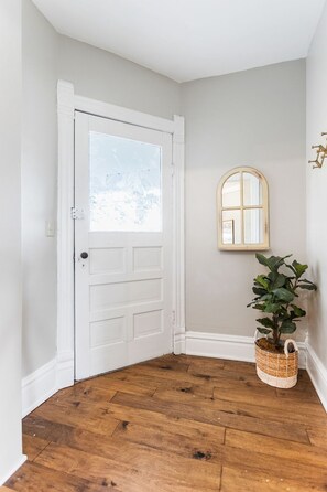 A hallway with a white door, wooden flooring, a small window, and a potted plant. - Farmhouse Retreat - 2 Acres, Fire Pit & Orchard Views (Fennville)