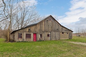A rustic wooden barn with a red door, large windows, and a sloped roof. - Farmhouse Retreat - 2 Acres, Fire Pit & Orchard Views (Fennville)