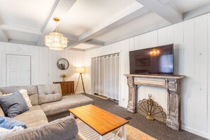 Ein Wohnzimmer mit einer Couch, einem Holztisch, einem Fernseher auf einem Kamin und einer Stehlampe.
