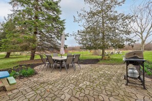 A patio with a stone table and chairs, a grill, and a blue table with a green stool. - Farmhouse Retreat - 2 Acres, Fire Pit & Orchard Views (Fennville)
