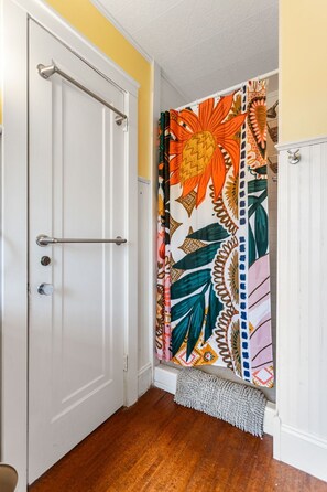 Um banheiro com porta branca, cortina de chuveiro com padrão floral e porta-toalhas branco.
