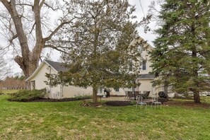A house with a large tree in the front yard, a patio with outdoor furniture, and a small garden area. - Farmhouse Retreat - 2 Acres, Fire Pit & Orchard Views (Fennville)