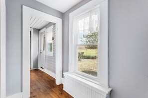 A hallway with a wooden floor, a white door, and a window with a view of a garden. - Farmhouse Retreat - 2 Acres, Fire Pit & Orchard Views (Fennville)