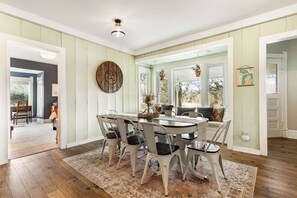 A dining area with a round table, white chairs, and a rustic wall clock. - Farmhouse Retreat - 2 Acres, Fire Pit & Orchard Views (Fennville)