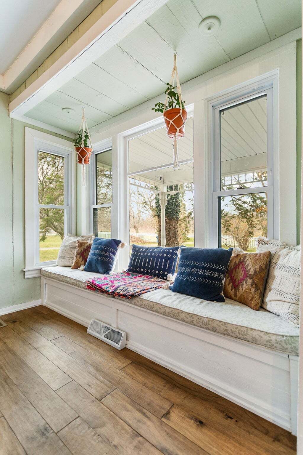 Une pièce chaleureuse avec un banc intégré, de grandes fenêtres et des plantes suspendues qui servent de décoration.