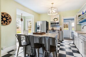 A kitchen with a central island, bar stools, a microwave, oven, and a hanging light fixture. - Farmhouse Retreat - 2 Acres, Fire Pit & Orchard Views (Fennville)