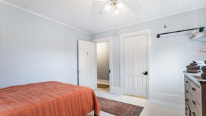 A bedroom with a bed, a dresser, a ceiling fan, and a door leading to another room.