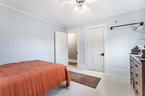 A bedroom with a bed, a dresser, a ceiling fan, and a door leading to another room. - Farmhouse Retreat - 2 Acres, Fire Pit & Orchard Views (Fennville)