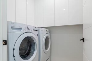 A laundry room with two front-loading washing machines and white cabinets. - Downtown Escape | Modern Stay with Pool (Austin)