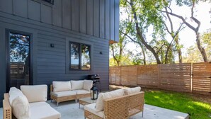 A patio with wicker furniture, a concrete table, and a wooden fence. - Downtown Escape | Modern Stay with Pool (Austin)