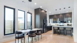 A modern kitchen with a central island, bar stools, and a dining area with a table and chairs. - Downtown Escape | Modern Stay with Pool (Austin)