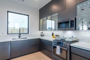 A modern kitchen with dark cabinets, a large window, a microwave, a stove, and a sink. - Downtown Escape | Modern Stay with Pool (Austin)