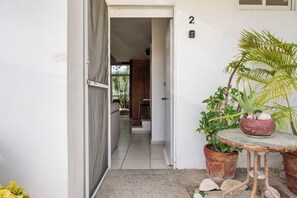 Un pasillo que da a una habitación con suelo de baldosas, una mesita con una planta en maceta y el número 2 en la pared.