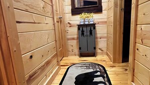 Ein schmaler Korridor mit Holzwänden, einem schwarz-weißen Teppich mit Bär-Silhouette, einem kleinen Schrank mit Sterndekoration und einem Fenster darüber.