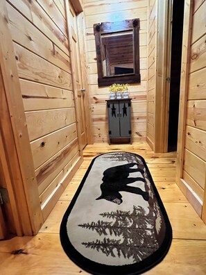 A narrow hallway with wooden walls, a black and white rug with a bear silhouette, a small cabinet with star decorations, and a window above. - Great Escape 2, charming 2 bed 2 bath cabin in Murphy, North Carolina (Murphy)