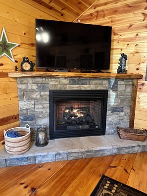 A fireplace with a stone surround, a television mounted above it, and a bear figurine on the mantel. - Easily Accessible charming 2bd 2ba cabin in Murphy, NC (Murphy)