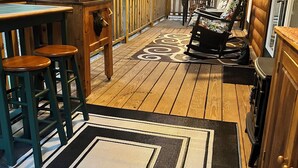 Eine überdachte Veranda mit Holzboden, einem Esstisch mit Stühlen, einer Couch und einer Küchenzeile.