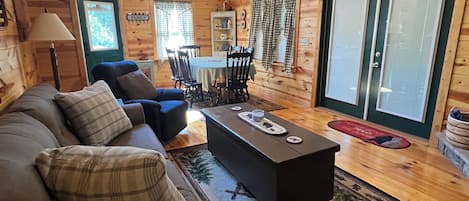 L’intérieur chaleureux d’un chalet comprend un canapé, une table basse, une table à manger, des chaises, des ventilateurs de plafond et une grande fenêtre.