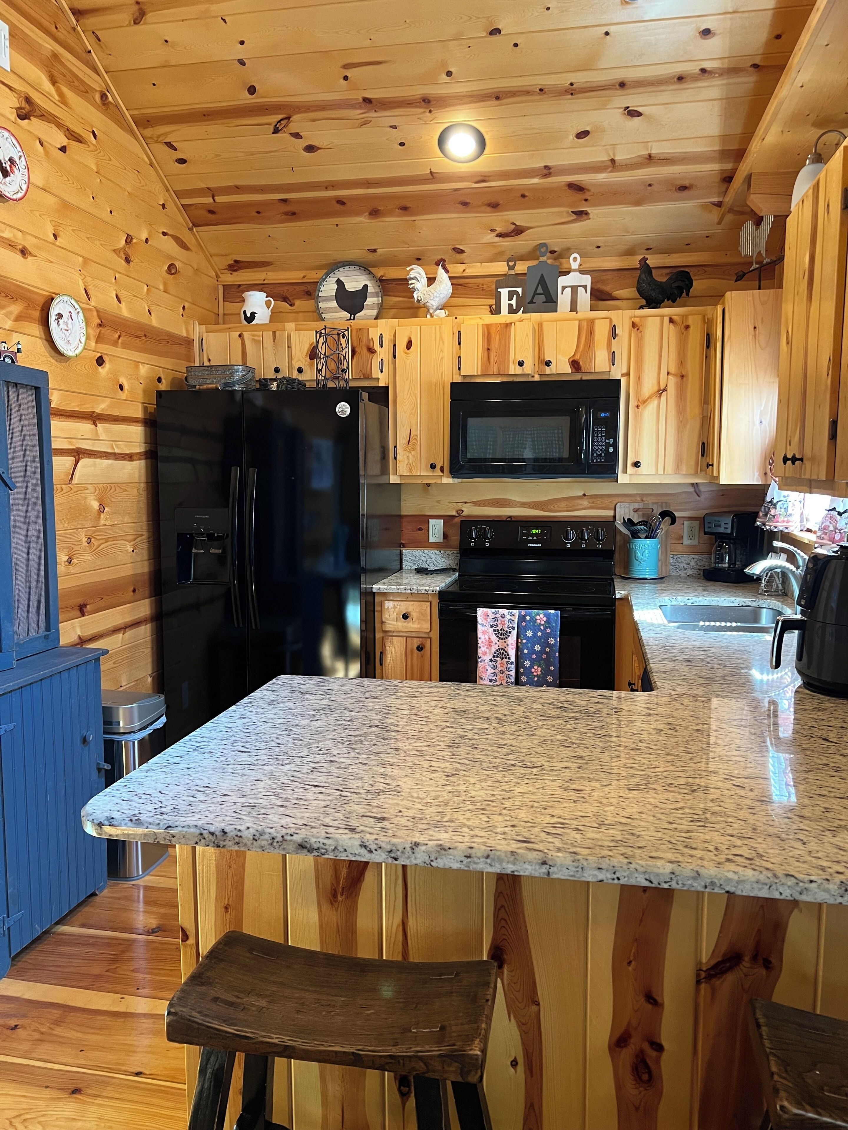 A kitchen with wooden cabinets, a black refrigerator, a microwave, and a granite countertop.