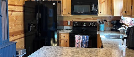 Una cocina con armarios de madera, un refrigerador negro, un microondas y una encimera de granito.