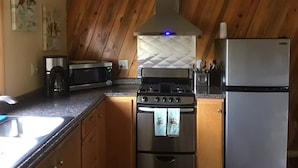 A kitchen with wooden walls, a stove, a microwave, a refrigerator, and a coffee maker.