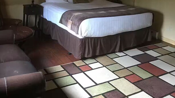 A bedroom with a bed, two bedside tables with lamps, a ceiling fan, a chair, and a colorful tiled floor.