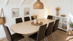 En spiseplads med et rundt bord, otte stole, en hængende lampe og billeder på væggen.