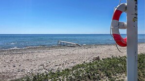 En redningskrans fastgjort til en stang, en trækonstruktion på stranden, og havet.