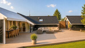 Et moderne udendørs område med terrasse, siddepladser og et overdækket spiseområde.