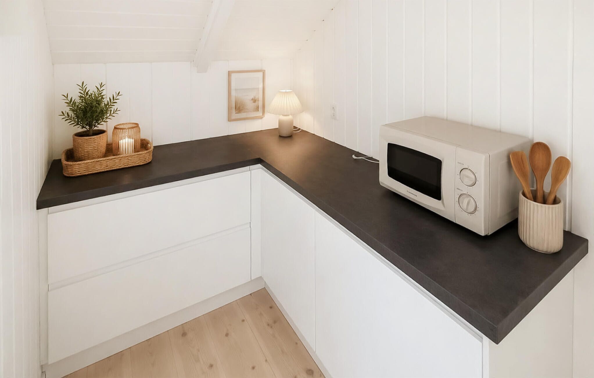 A kitchen with white cabinets, a dark countertop, a microwave, a lamp, and a plant.