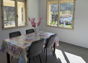 En spiseplads med et bord dækket af en dug med bladmotiver, omgivet af stole, og en vase med lyserøde blomster.