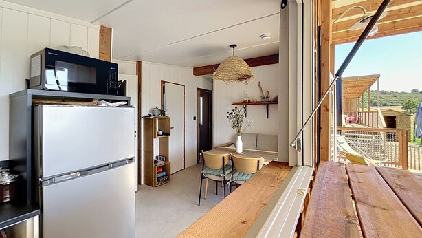 A compact kitchen with a refrigerator, microwave, and wooden dining table. - Beach house with private parking - 4 guests (Saint-Pair-sur-Mer)