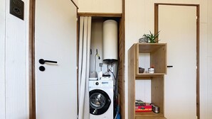 A laundry room with a washing machine, a drying rack, and a wooden shelf with board games. - Beach house with private parking - 4 guests (Saint-Pair-sur-Mer)